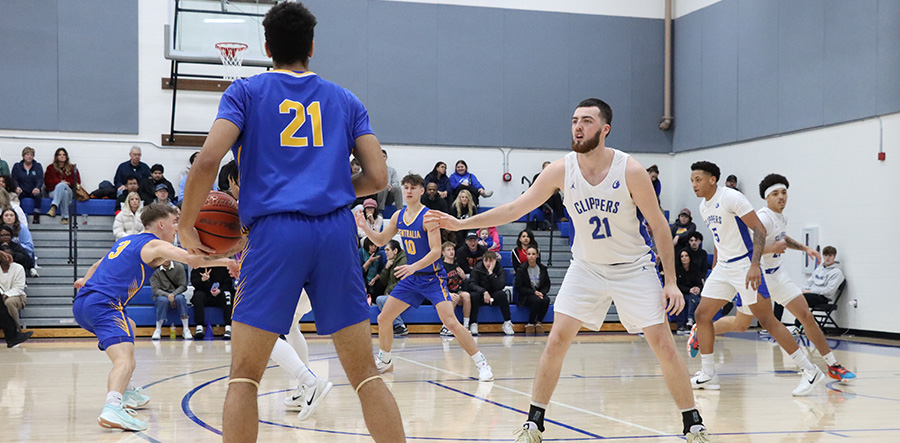 Basketball player surveys court as he holds basketball looking to pass while opposing player stands in his way.